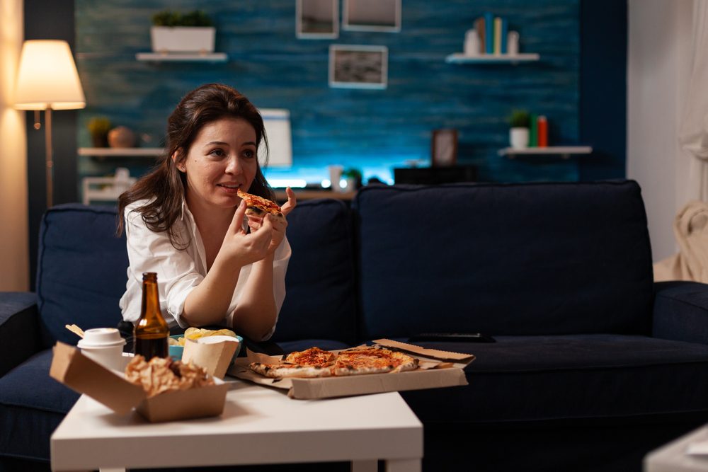 Žena gleda TV i jede picu, grickalice, pije pivo...