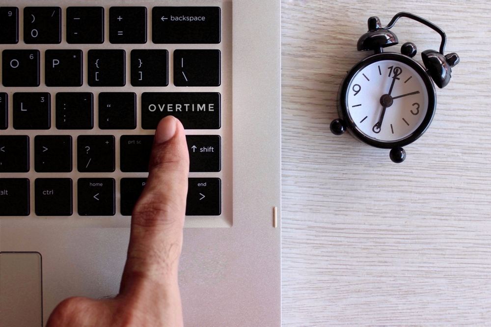 Tastatura na kojoj na jednoj od dirki piše overtime, sa desne strane na stolu je budilnik.