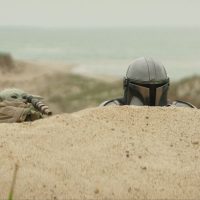 Star wars, grogu i mandalorac u pustinji iza peščane dine.