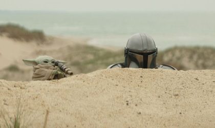 Star wars, grogu i mandalorac u pustinji iza peščane dine.