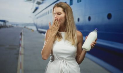 Žena koja se zagrcnula i pokušava da iskašlje zalutali gutljaj. U jednoj ruci drži flašu sa mlekom.