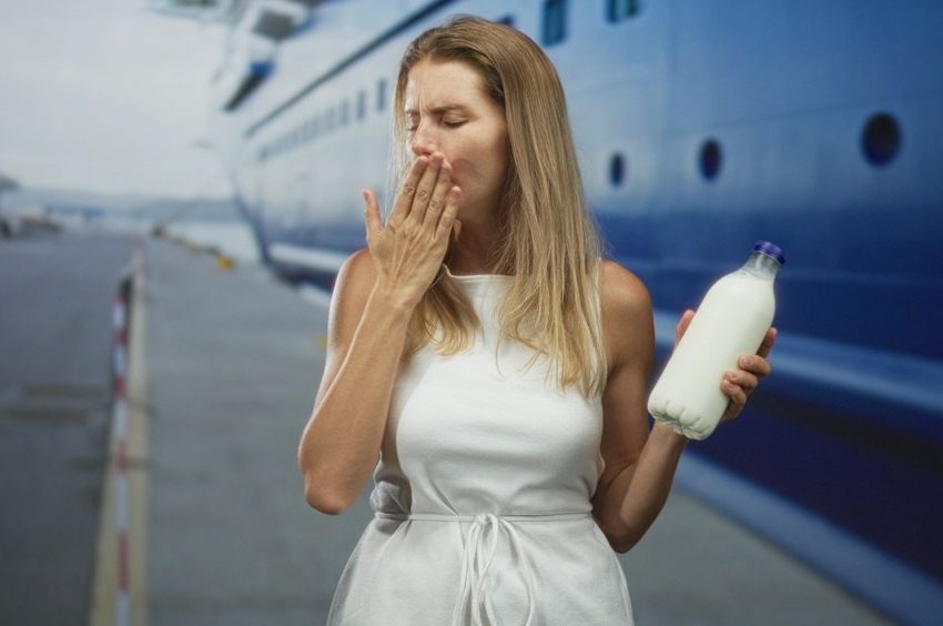 Žena koja se zagrcnula i pokušava da iskašlje zalutali gutljaj. U jednoj ruci drži flašu sa mlekom.