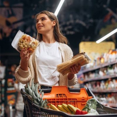 Žena drži namirnice u rukama pored korpe u supermarketu.