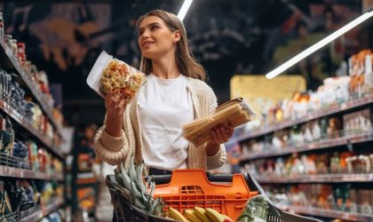 Žena drži namirnice u rukama pored korpe u supermarketu.