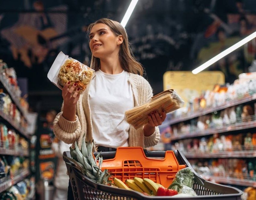 Žena drži namirnice u rukama pored korpe u supermarketu.