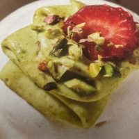 Mini pavlova na tanjiru, ukrašena lomljenim pistaćima i listićima jagode.
