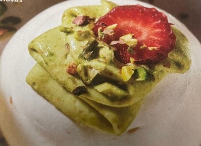 Mini pavlova na tanjiru, ukrašena lomljenim pistaćima i listićima jagode.