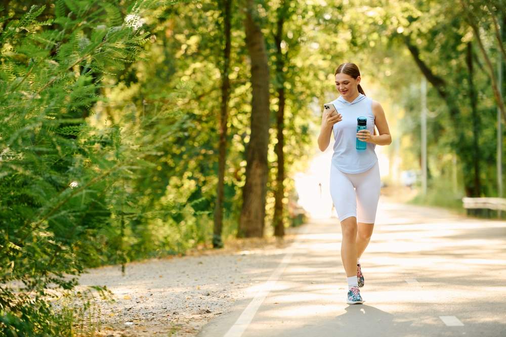 Žena u sportskoj opremi hoda po stazi u po&scaron;umljnom predelu.