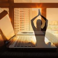 Fotografija ilustracija, lap top na stolu, kroz prozor se vidi grad. Preko fotografije je ilustracija žene koja radi jogu.