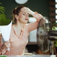 Žena u kancelariji, bori se sa toplotom, ne oseća se dobro, stavila je ventilator na sto.