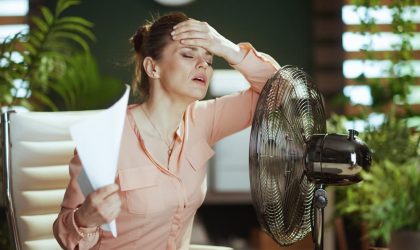 Žena u kancelariji, bori se sa toplotom, ne oseća se dobro, stavila je ventilator na sto.