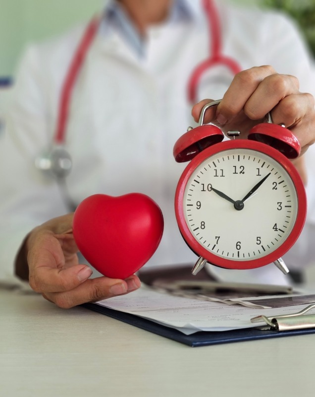 Doktor u ordinaciji u jednoj ruci drži model srca, a u drugoj budilnik.