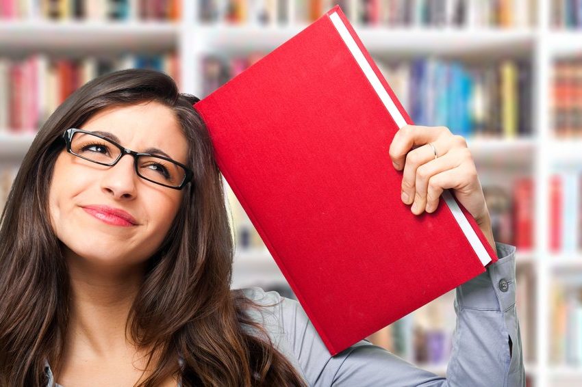 Žena u biblioteci naslonila je knjigu na glavu i kao da promišlja i da je došla do nekog zaključka.