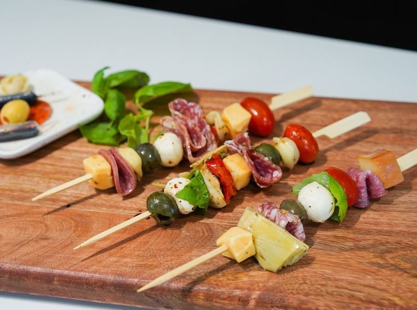 Antipasto ražnjići. Na drvene štapiće nataknut je čeri paradajz, krastavac, sir, masline i dr. Postavljeni su na dasci.