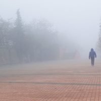 Čovek koji se vidi s leđa, nosi jaknu sa kapuljačom. Hoda pločnikom. Okolo i u daljini je magla.
