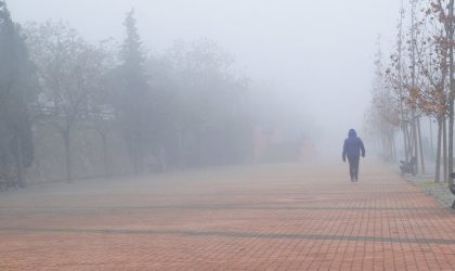 Čovek koji se vidi s leđa, nosi jaknu sa kapuljačom. Hoda pločnikom. Okolo i u daljini je magla.