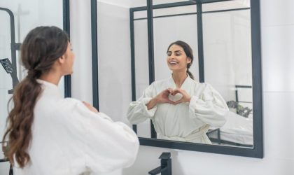Devojka se ogleda u ogledalu ispred grudi je rukama napravila znak srce.