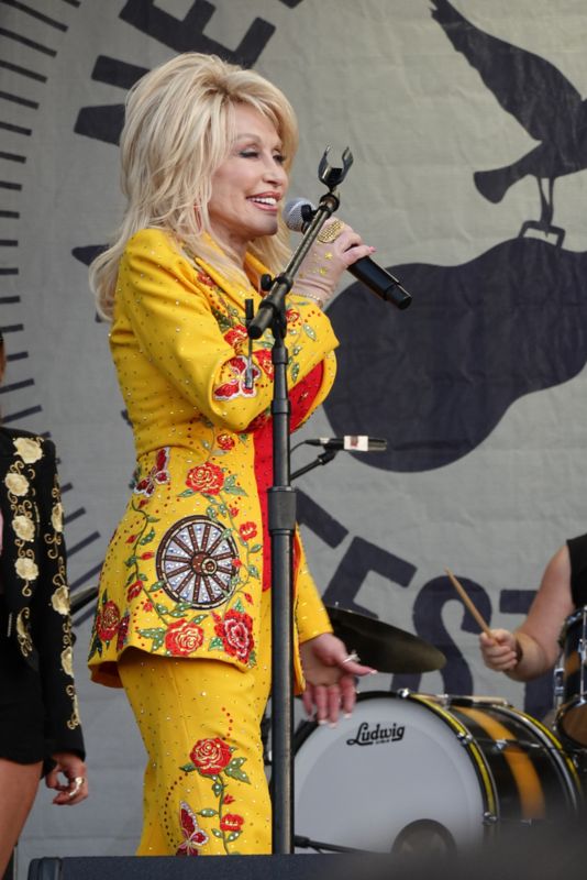 Doli Parton unstarijem dobu, nosi jarko žuto odelo sa raznobojnim aplikacijama, cveća, leptirova itd.