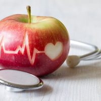 Jabuka na kojoj je urezana linija EKG-a i simbol srca. Na stolu pored jabuke je simbolično i stetoskop.