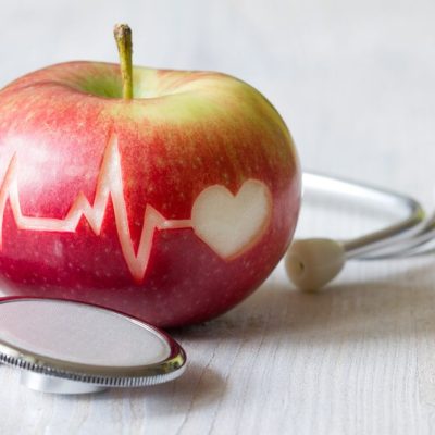 Jabuka na kojoj je urezana linija EKG-a i simbol srca. Na stolu pored jabuke je simbolično i stetoskop.