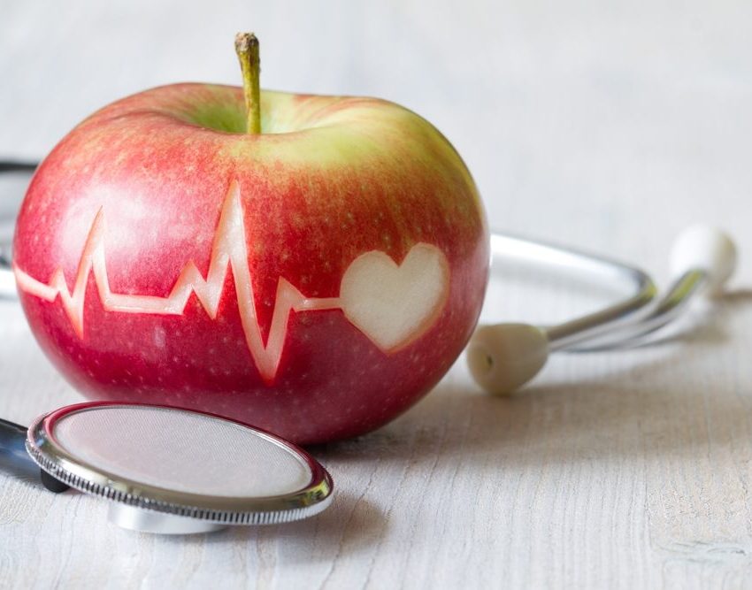 Jabuka na kojoj je urezana linija EKG-a i simbol srca. Na stolu pored jabuke je simbolično i stetoskop.