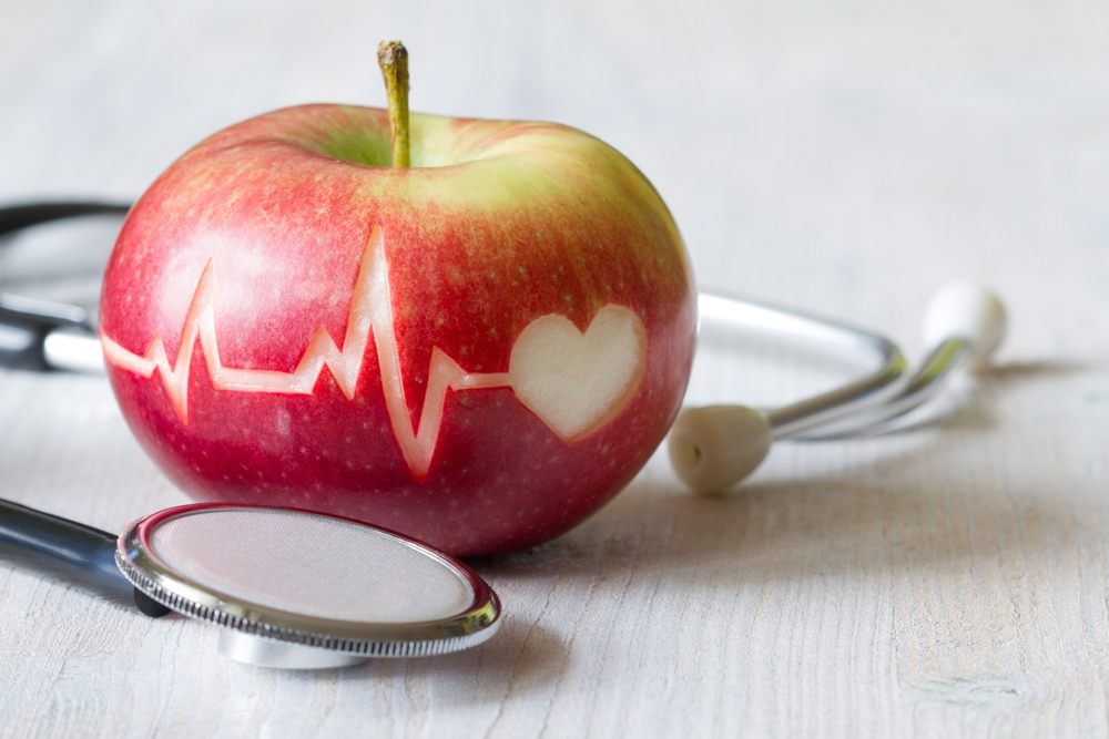 Jabuka na kojoj je urezana linija EKG-a i simbol srca. Na stolu pored jabuke je simbolično i stetoskop.
