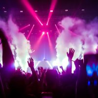 Velika grupa ljudi sa rukama podignutim uvis, pod svetlima raznih reflektora igra uz muziku koju pušta DJ.