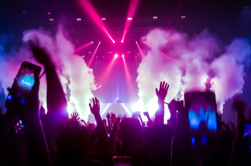 Velika grupa ljudi sa rukama podignutim uvis, pod svetlima raznih reflektora igra uz muziku koju pušta DJ.