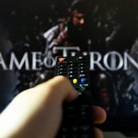 Na TV-u je špica za seriju Game of thrones. Daljinski upravljač u ruci, uperen ka TV-u.