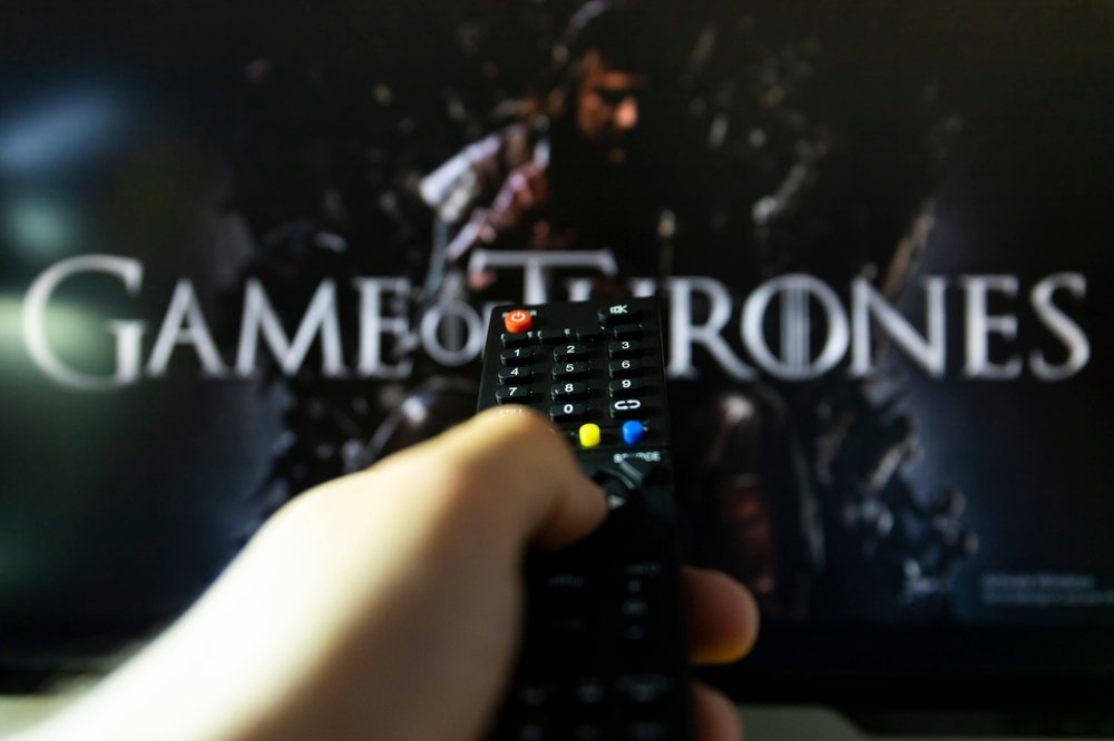 Na TV-u je špica za seriju Game of thrones. Daljinski upravljač u ruci, uperen ka TV-u.