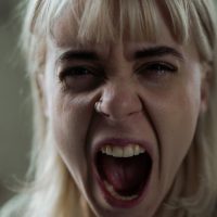 Žena jako otvorenih usta, vidi se lice sa izraženom grimasom, vrišti.