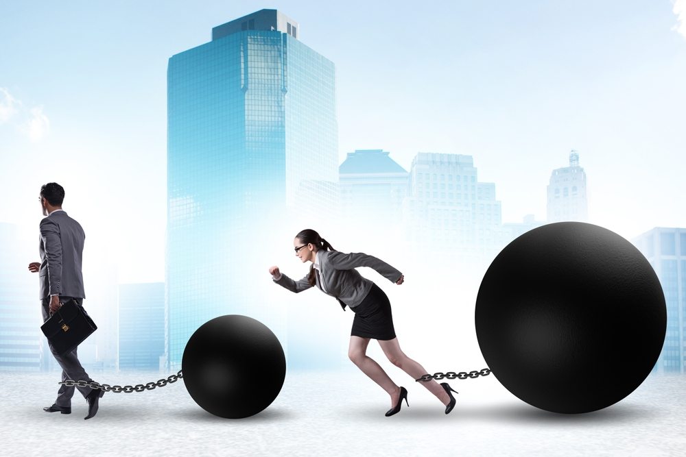 Ilustracija žene koja ima veliku lancem privezanu kuglu za članak, kao da trči, juri da stigne muškarca koji ima manju kuglu isto vezanu za članak, ali je ispred nje i lagano se kreće.