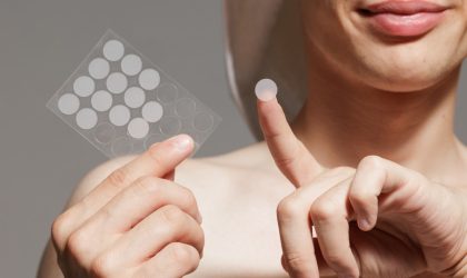 Žena koja drži mali silikonski flaster na prstu, a u drugoj ruci joj je folija na koju je nalepljeno više takvih flasterčića.